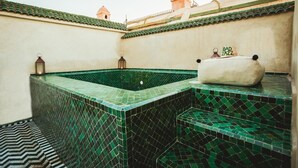 Une piscine sur le toit, avec des carreaux de mosaïque verts, un banc rembourré et des lanternes.