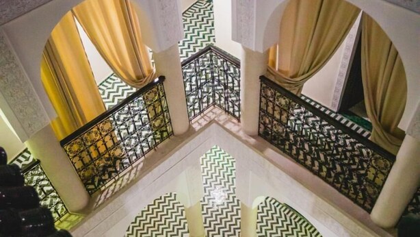 Une cour avec un sol à motifs, une fontaine centrale et une balustrade au décor géométrique.