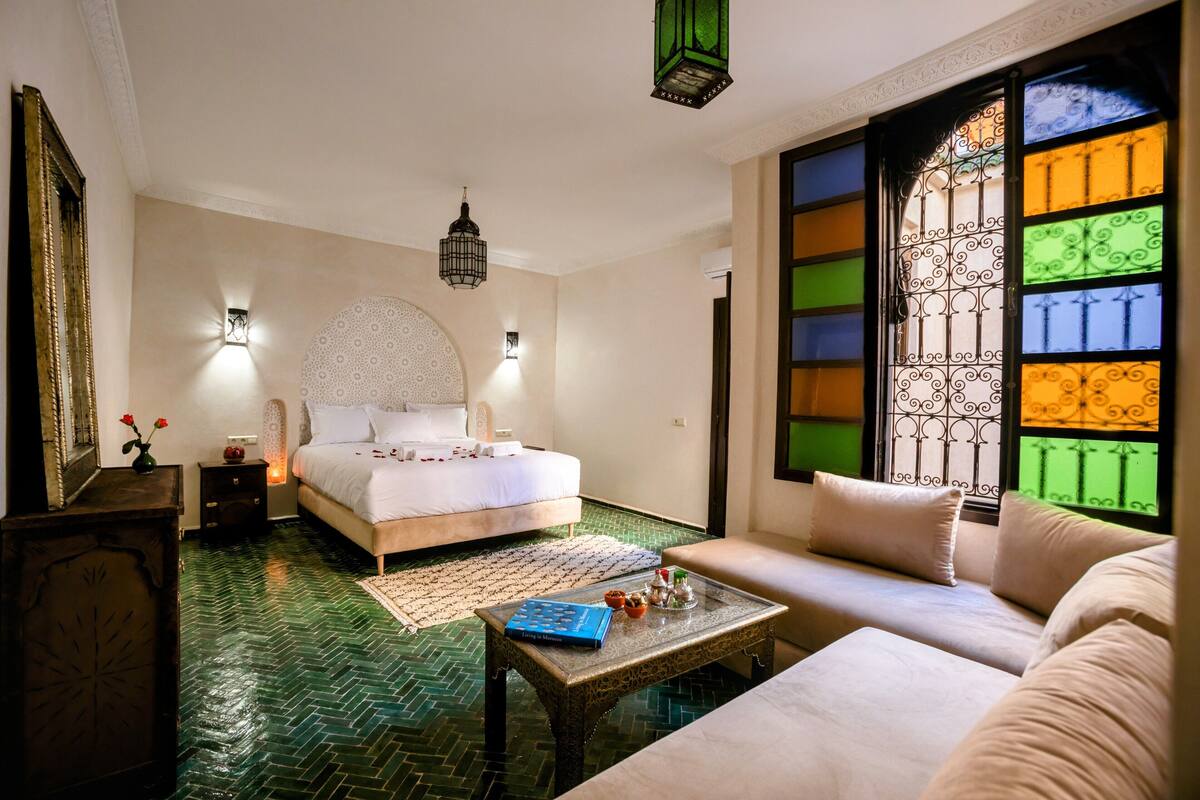 Quarto com cama, sofá, mesa de centro e janela com vitrais coloridos.