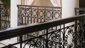 Un balcon orné de balustrades en fer forgé, un rideau beige et un mur blanc aux motifs complexes.