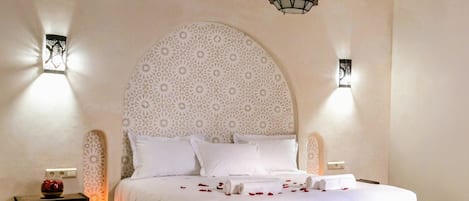 A bedroom with a large bed, two bedside tables, a decorative ceiling light, and patterned wall decor.