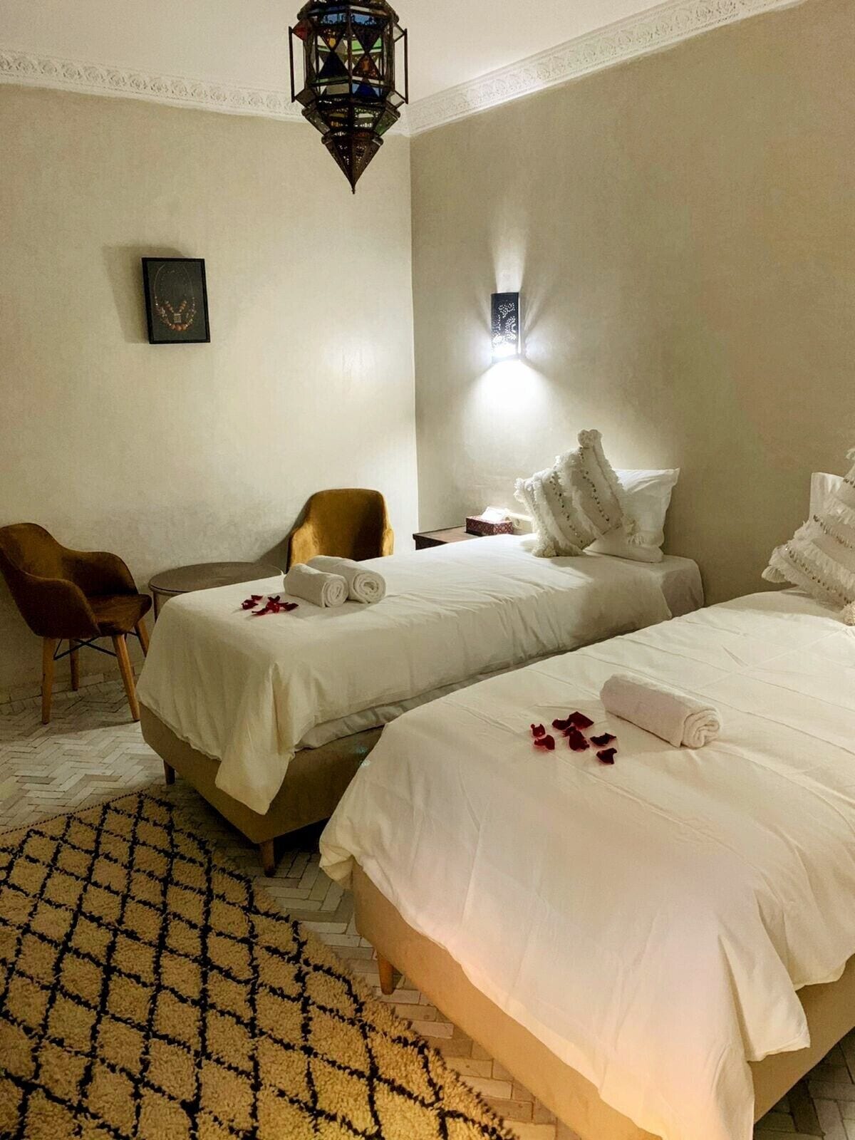 Habitación de hotel con dos camas, una silla, una mesita y una lámpara de pared decorativa.