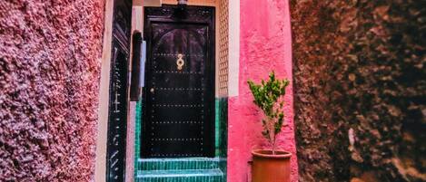 Une ruelle étroite avec un immeuble doté d’une porte noire et d’un petit balcon surmonté d’un toit en tuiles.