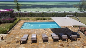 A pool area with lounge chairs and a view of the ocean.