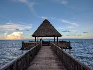 Un muelle de madera que conduce a una estructura con techo de paja, con vista al mar.