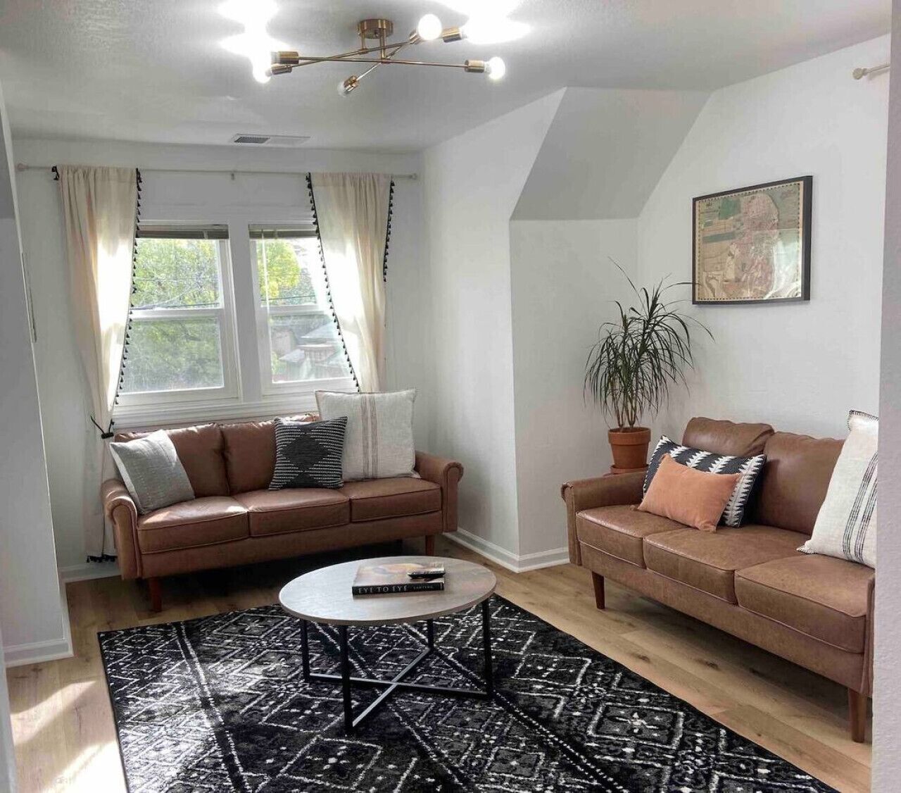 A living room with two brown leather sofas, a round coffee table, a black patterned rug, and a ceiling light fixture.