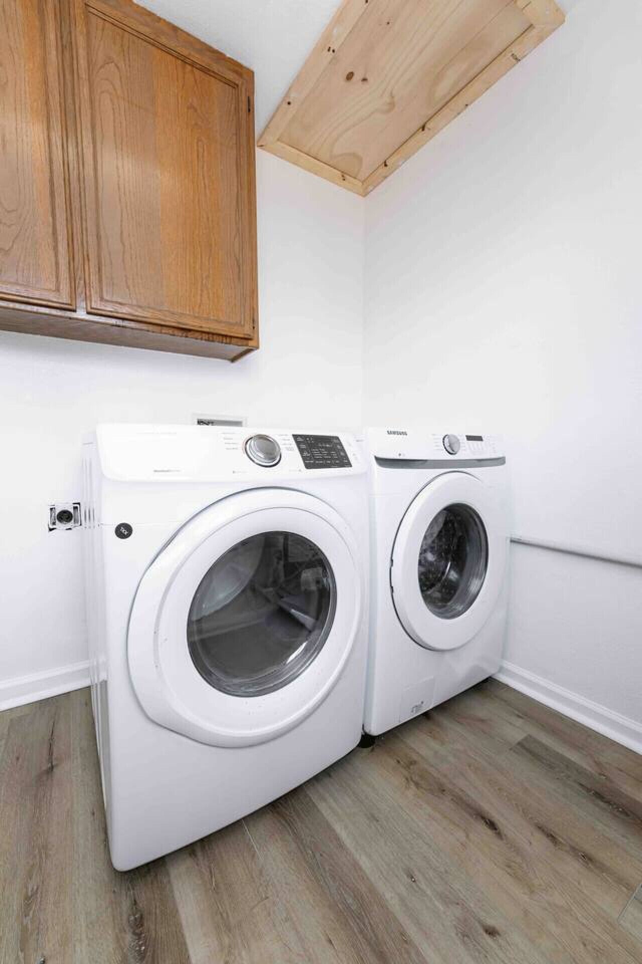 A laundry room with two white front-loading washing machines, wooden cabinets, and a wooden ceiling.