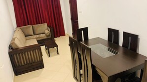 A dining area with a dark wooden table and matching chairs, a beige sofa, and a red curtain in the background.