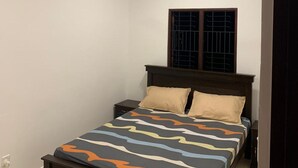 A bedroom with a bed, a ceiling fan, a window with bars, and a power outlet.
