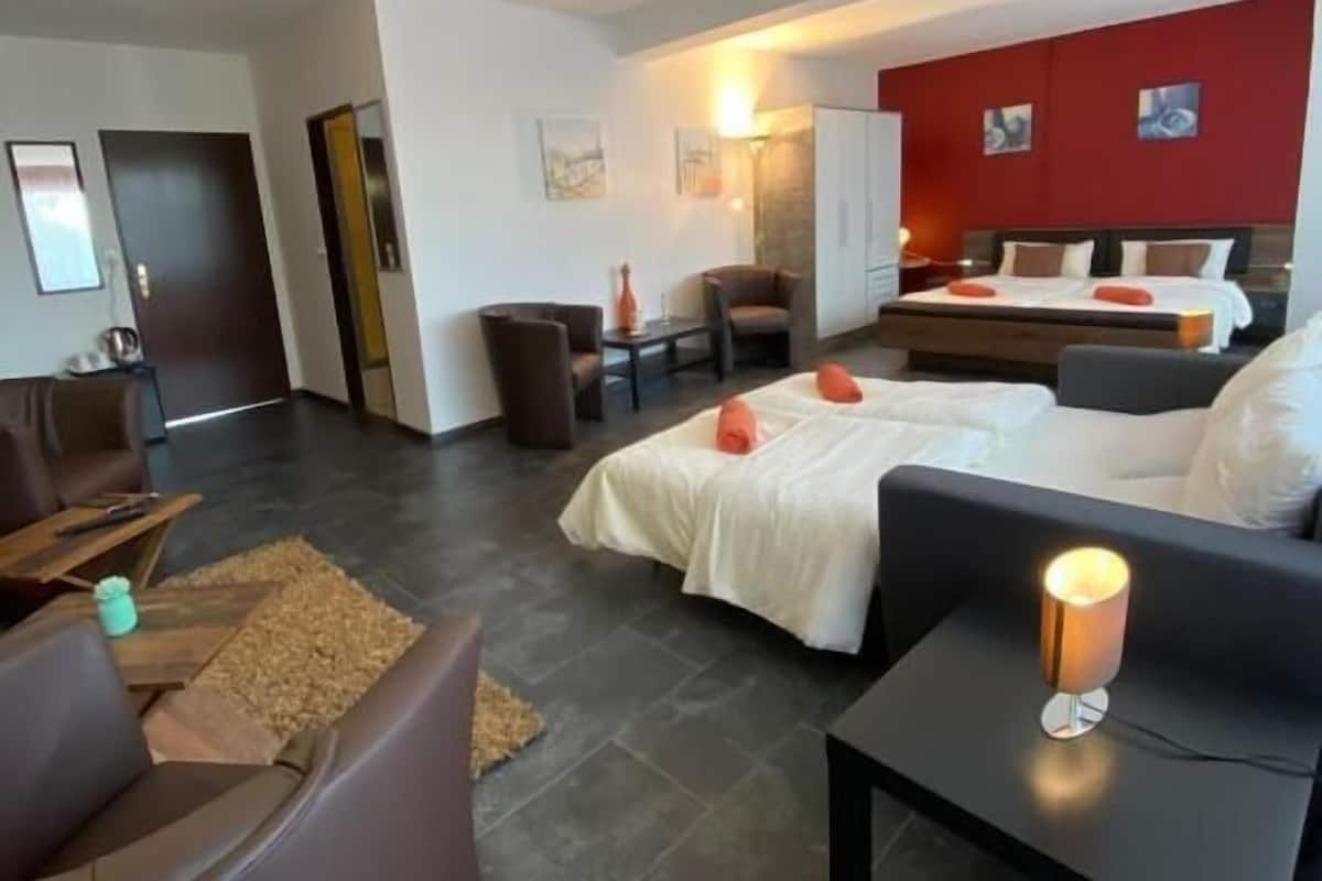 A modern hotel room with a large bed, a sofa, a small table with a lamp, and a chair.