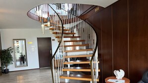 A modern spiral staircase with wooden steps and metal railings, a potted plant, and a leather chair in a room with wooden flooring and a large mirror. - Sonnenstrand Hotel (Butjadingen)