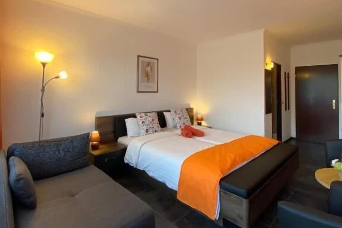 A hotel room with a bed, a sofa, a small table, and a nightstand.