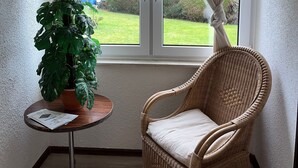 A corner room with a wicker chair, a small table with a plant, and a window with curtains. - Sonnenstrand Hotel (Butjadingen)