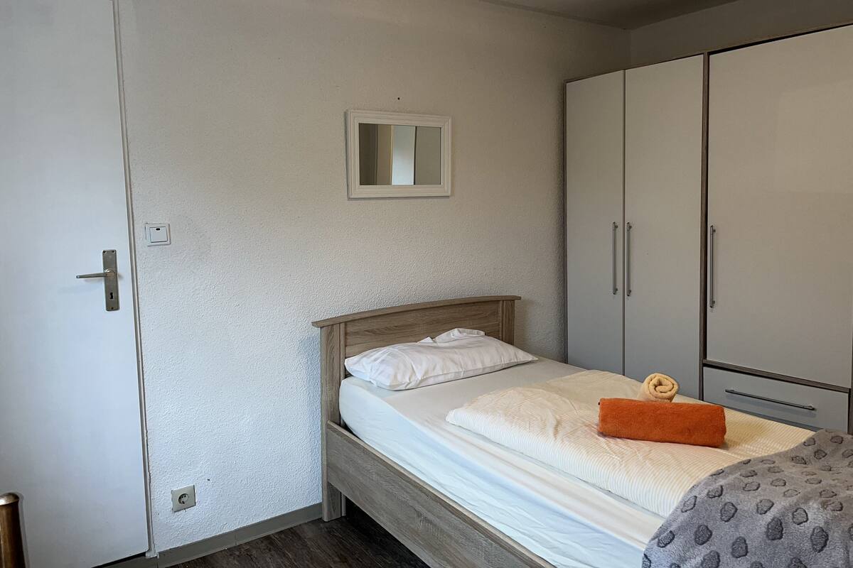 A bedroom with a wooden bed, white bedding, a small mirror, and a wardrobe.