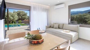 Ein modernes Wohnzimmer mit einem Glastisch, einer Couch und Blick auf einen Swimmingpool und Bäume.