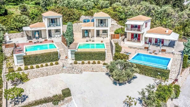 Una villa moderna con dos piscinas, fachada de piedra y abundante vegetación.