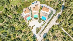 Vista aérea de un complejo turístico con varias edificaciones, piscinas y una zona boscosa circundante.