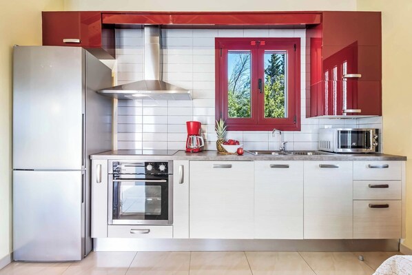 Une cuisine moderne dotée d’appareils électroménagers en acier inoxydable, d’une fenêtre à cadre rouge et de meubles blancs.