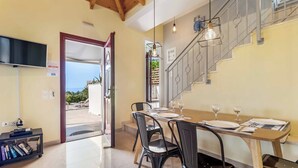Un comedor con una mesa de madera dispuesta para dos personas, sillas negras y una escalera con barandillas de metal.