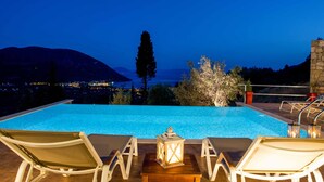 Zona junto a la piscina con sillones de descanso y vista al mar al atardecer.