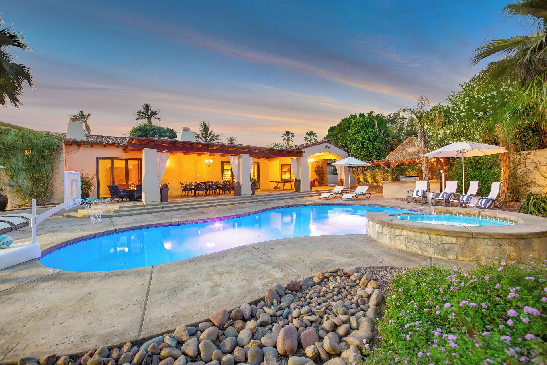 A pool area with a basketball hoop, lounge chairs, and a dining area with a table and chairs.