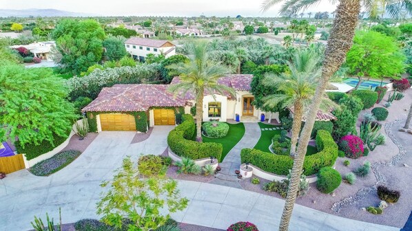 A residential area with a house featuring a tiled roof, a garage, and a well-maintained garden with various plants and a lawn. - Virtual Golf, Pickle+Volley+Basketball+Putting Green+Theatre+Gameroom+Ping Pong (Indio)