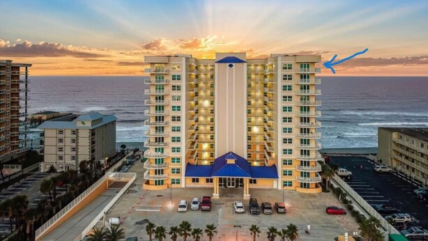 A high-rise hotel with multiple balconies, a central entrance, and a parking area in front. - Beachview Luxury Condo Decks & Views (Daytona Beach)