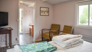 Een slaapkamer met een bed, een stoel, een televisiescherm en een raam.