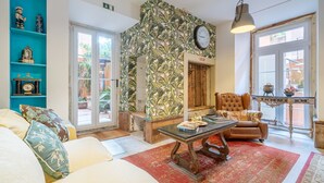Un salón acogedor con alfombra roja, una mesa de centro de madera, un sillón marrón y un mueble de estanterías color turquesa con objetos decorativos.