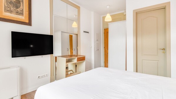 A hotel room with a bed, a TV mounted on the wall, a wooden dresser, and a door.