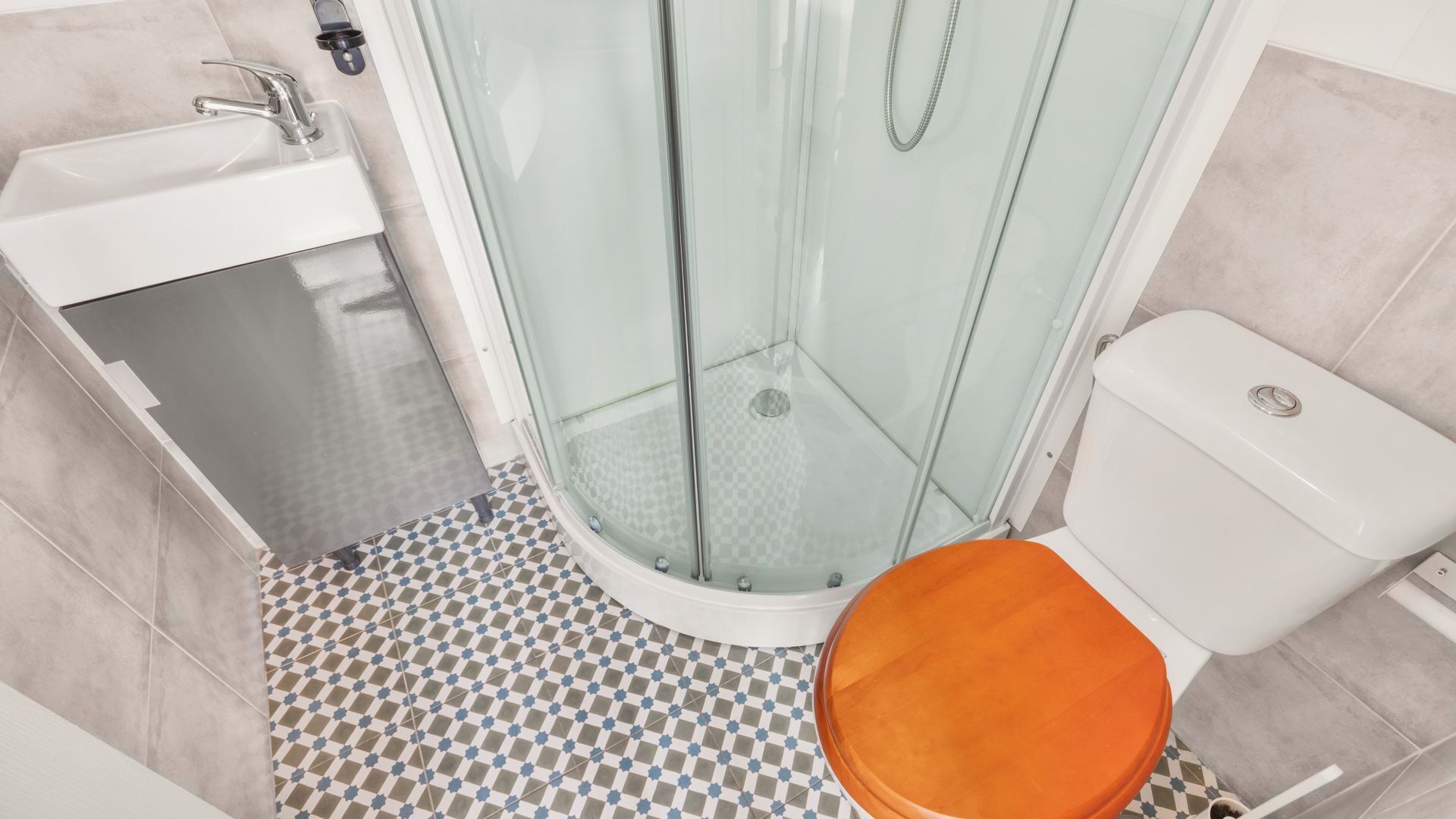 A bathroom with a glass shower enclosure, a white sink, a toilet, and a checkered floor.