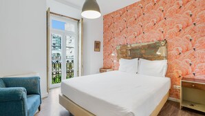 A bedroom with a large bed, a blue armchair, a wooden headboard, and a window with a view of buildings.