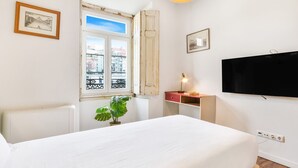 Habitación de hotel con cama, escritorio, televisión, ventana y vista a edificios, además de una planta.