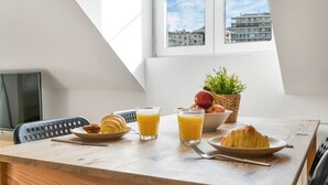 Desayuno con cruasanes, fruta y jugo de naranja sobre una mesa de madera cerca de una ventana con vista a la ciudad.