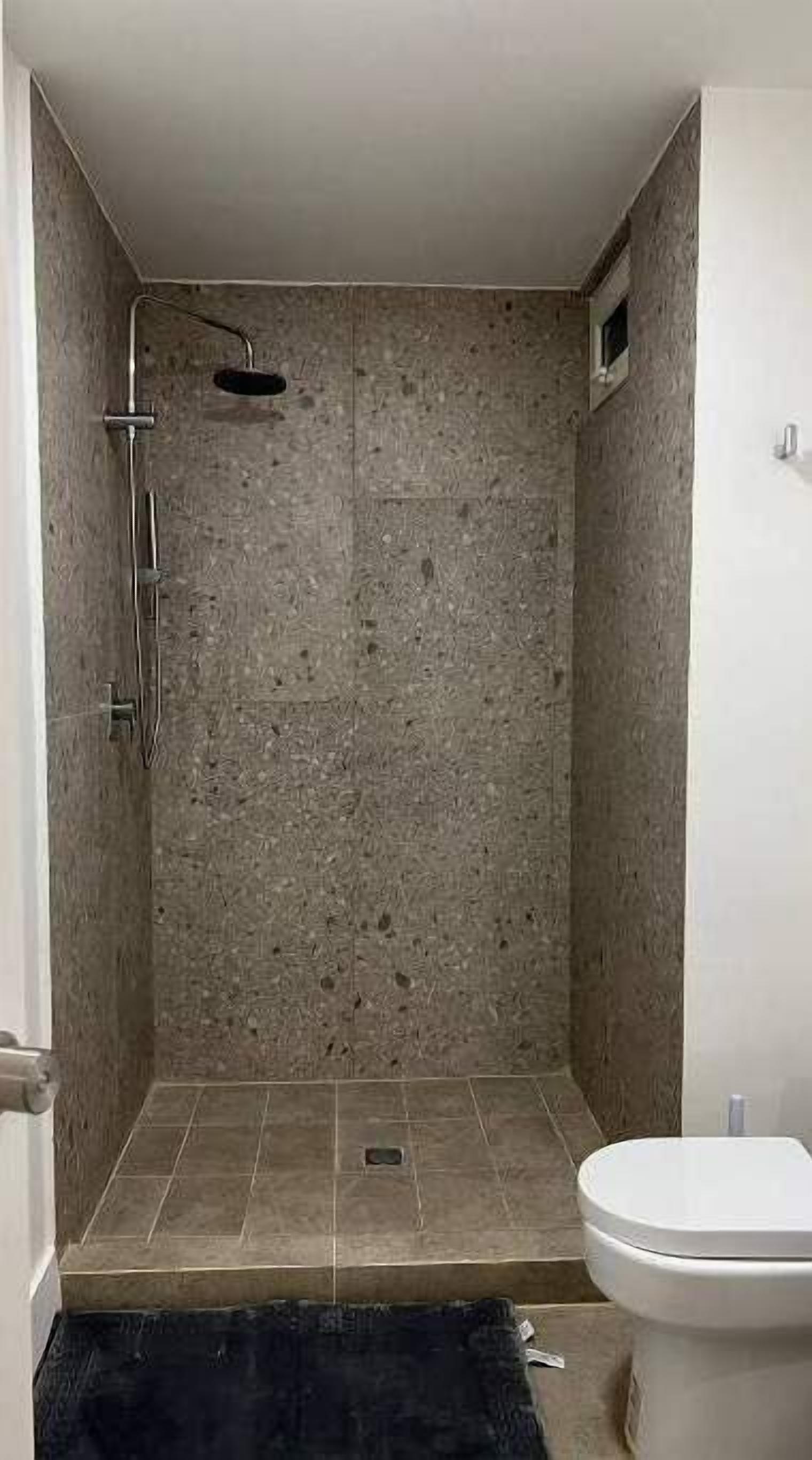 Un baño con ducha, paredes de azulejos y un inodoro.