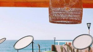 Zona salotto all'aperto con vista mare, con tavolo, sedie e lampadario.
