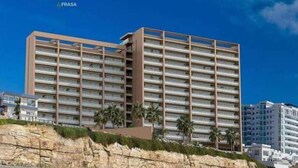 Un hotel moderno con diversi piani, situato vicino a una spiaggia con un litorale roccioso.