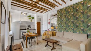 A modern living room with a sofa, a wooden coffee table, and a dining area with a table and chairs. There is a kitchen in the background with a microwave and a refrigerator. - The Indy House | Room 504 by LovelyStay (Lisboa)