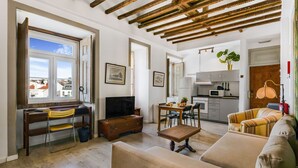 A living room with a sofa, a TV, a dining table with chairs, and a kitchen area with cabinets and a microwave. - The Indy House | Room 504 by LovelyStay (Lisboa)