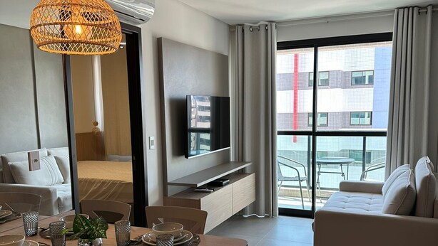 Une chambre d’hôtel moderne dotée d’un coin repas, d’un canapé, d’une télévision et d’un balcon offrant une vue sur la ville.
