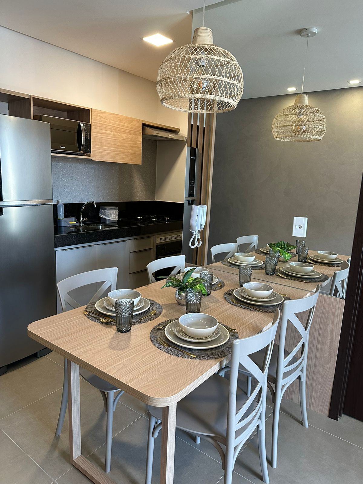 Een moderne keuken met een eethoek. Uiterst geschikt met een koelkast van roestvrij staal, een magnetron, een fornuis en een spoelbak. De eettafel is gedekt met borden, kommen en glazen. Er staan witte stoelen rondom de tafel.