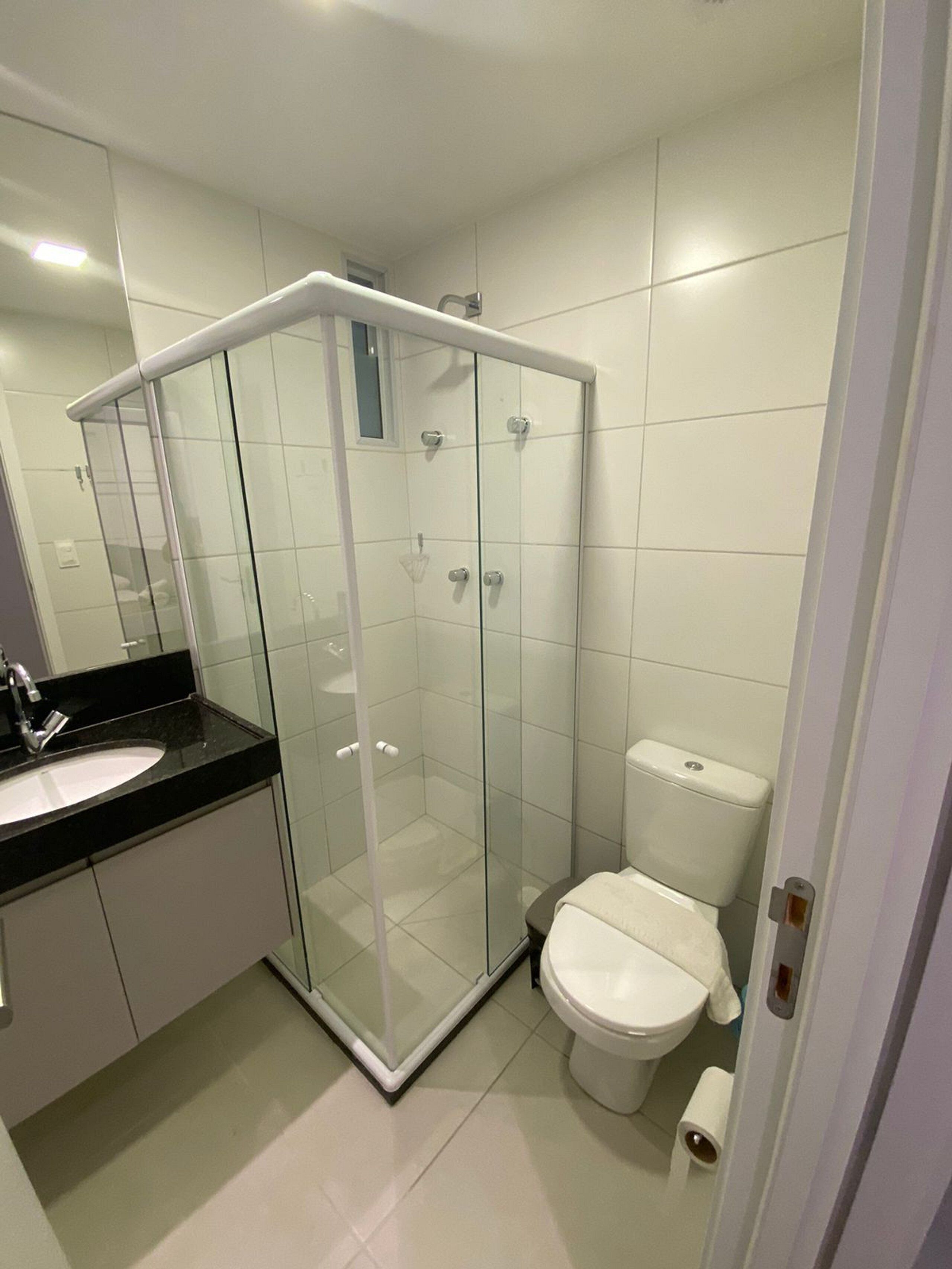Un baño moderno con ducha envuelta en vidrio, inodoro blanco y lavamanos sobre encimera negra.