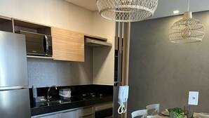 Une cuisine moderne avec un coin repas. Elle comprend un réfrigérateur en acier inoxydable, un four à micro-ondes, une cuisinière et un évier. Deux lampes suspendues et une plante en pot décorent la table à manger.