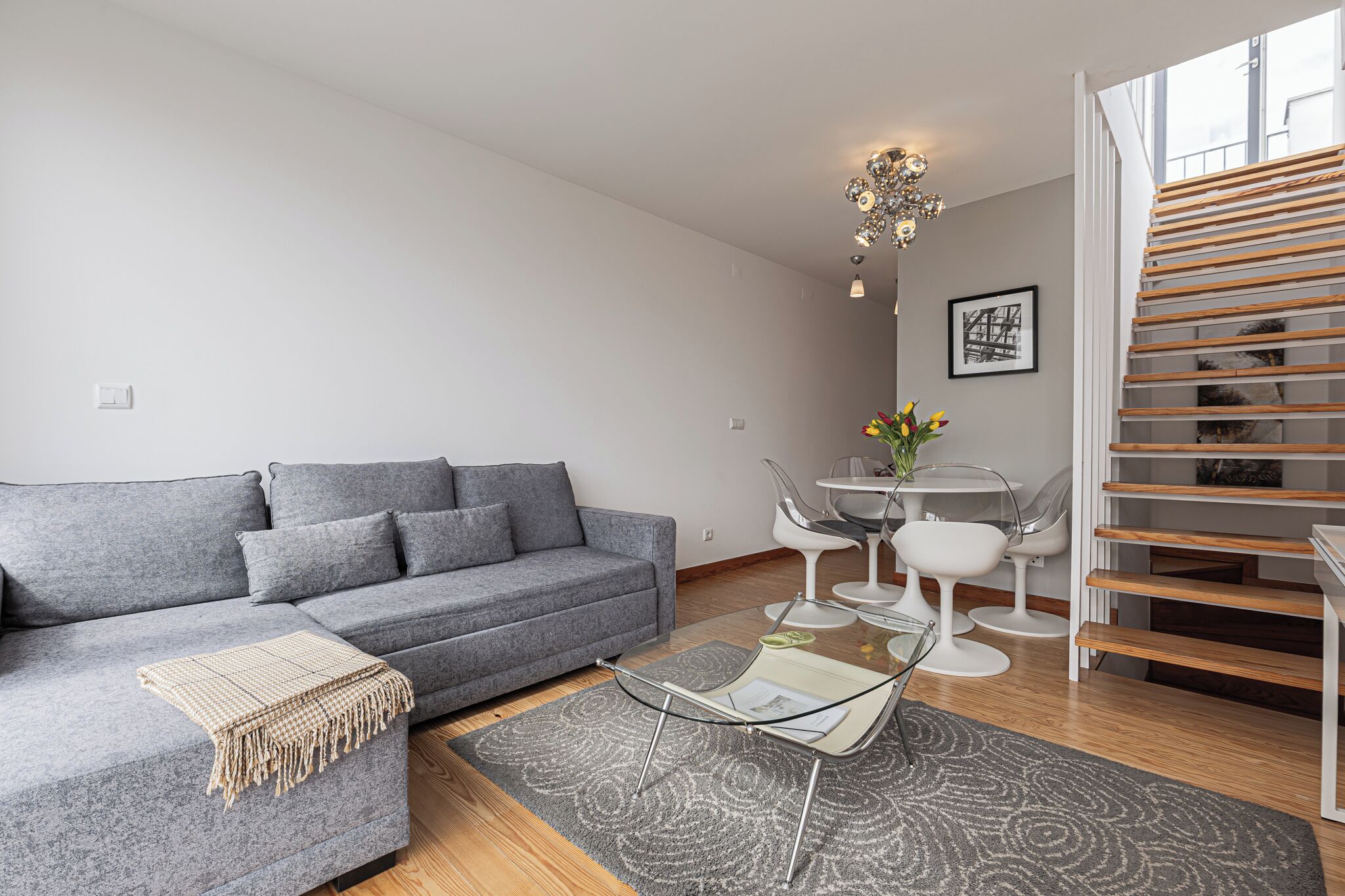 A modern living room with a grey sofa, a glass coffee table, and a staircase with wooden steps.
