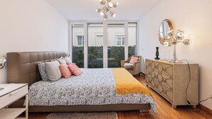 A bedroom with a bed, bedside table, dresser, and a large window. - Barbadinhos Apartments in Lisbon Historic (Lisbon)
