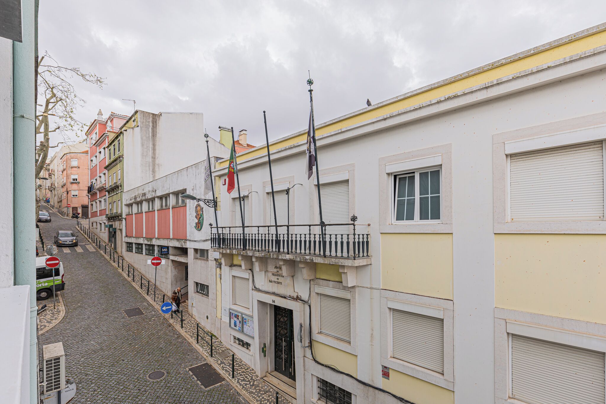 Une ruelle étroite pavée, bordée d’immeubles, avec un autobus et un piéton.