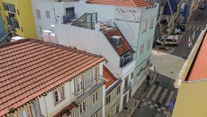 A multi-story building with a red-tiled roof, balconies, and a street view with a tram and parked cars. - Barbadinhos Apartments in Lisbon Historic (Lisbon)