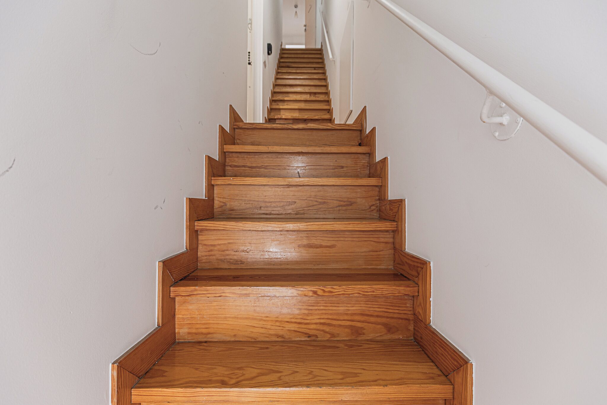 A wooden staircase with a handrail on the right side, leading to an upper floor.