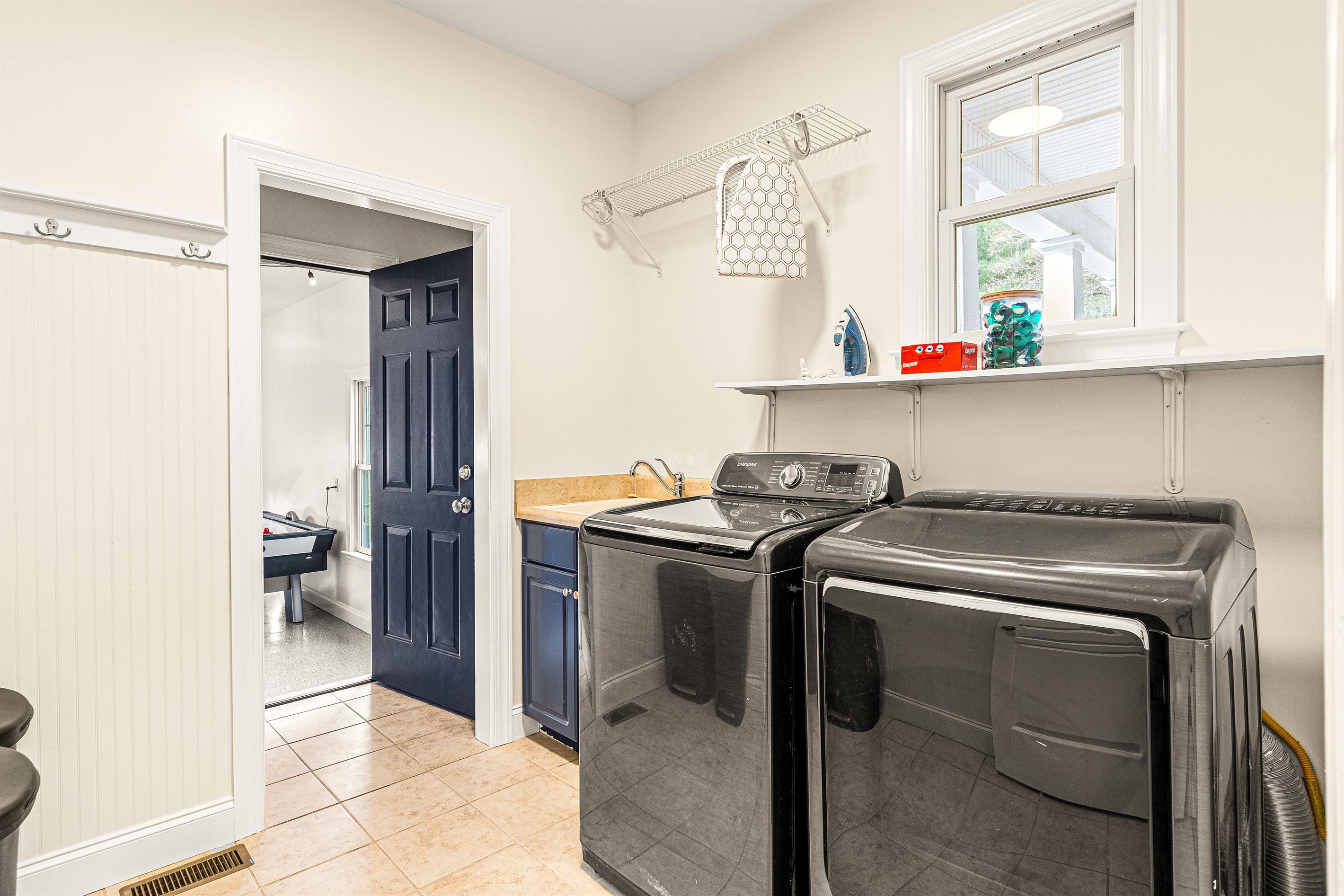 A laundry room with two front-loading washing machines, a drying rack, and a window above the sink.