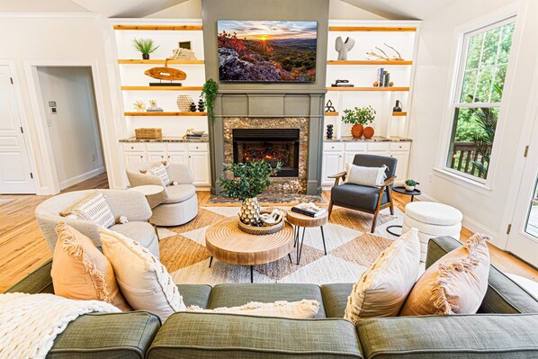 Un salón amplio con chimenea, asientos cómodos y un televisor grande montado sobre él.